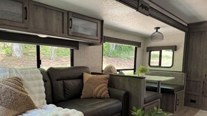 A cozy RV interior with a sectional sofa, a small dining table, and a kitchenette area. - Private one-of-a-kind Camping experience! Hot Tub! (Narvon)