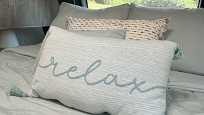 A bed with two pillows, one with the word "relax" embroidered on it, and a view of greenery outside a window. - Private one-of-a-kind Camping experience! Hot Tub! (Narvon)