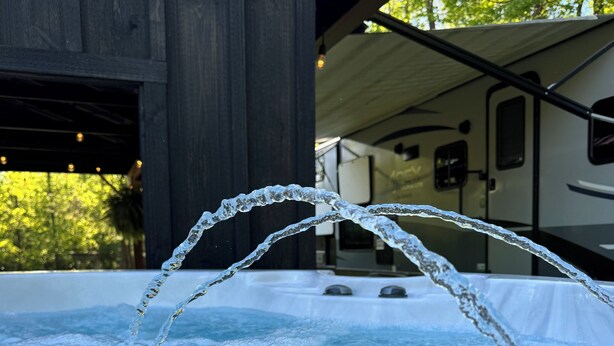 A hot tub with water jets in a covered outdoor area, with a building and trees in the background. - Private one-of-a-kind Camping experience! Hot Tub! (Narvon)