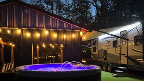 A hot tub with a blue light, a covered patio area with string lights, and a camper RV in the background. - Private one-of-a-kind Camping experience! Hot Tub! (Narvon)