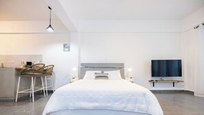 Ein modernes Schlafzimmer mit einem großen Bett, zwei Nachttischen, einem an der Wand montierten Fernseher und einer kleinen Küchenzeile mit Barhocker.