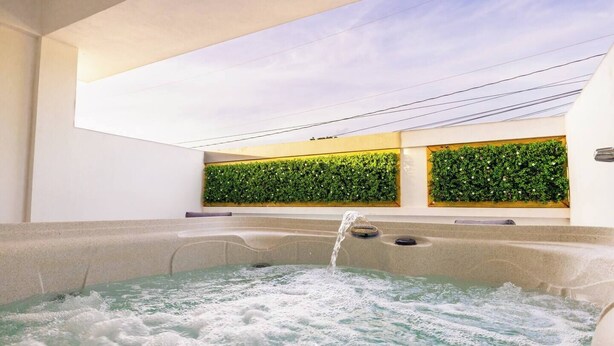 Ein Whirlpool mit Wasserstrahlen, ein Dachfenster und eine grüne Wand mit Pflanzen.