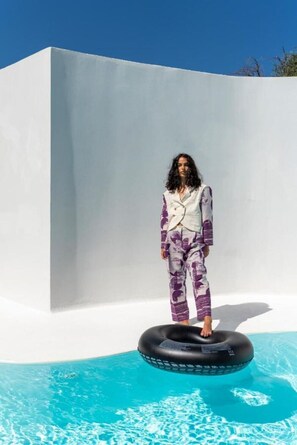 Eine Person steht in einem schwarzen Luftmatratzenring in einem Pool mit klarem, blauem Wasser, gekleidet in ein weißes und lilafarbenes Outfit.