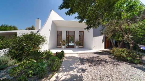 Una casa moderna blanca amb un teulat triangular, un porxo amb plantes en testos i un carrer d'accés de grava.