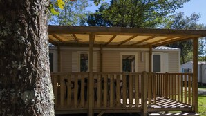 Una terraza de madera con una pérgola, un espacio cubierto pequeño y un escalón que lleva a una puerta.