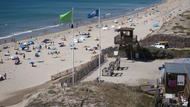 Una playa con una torre de salvavidas, sombrillas y gente disfrutando.
