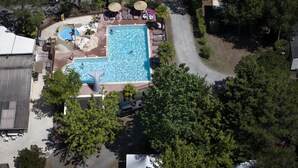 Vista aérea de un resort con piscina central, sillas de descanso y una cascada.
