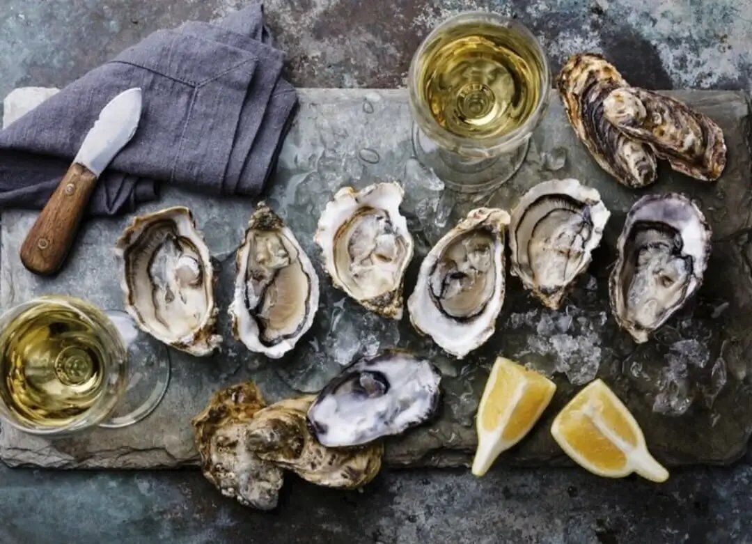 A selection of oysters on ice with a knife, a cloth, and glasses of white wine.