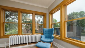 Ein Zimmer mit großen Fenstern, einem Heizkörper, einem blauen Sessel und einem Holzboden.