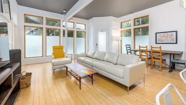 Ein modernes Wohnzimmer mit einem weißen Sofa, einem Holztisch und einem Essbereich mit Tisch und Stühlen.