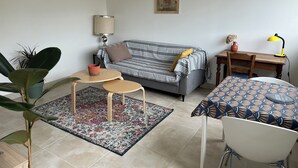 A living room with a sofa, a coffee table, a dining table with chairs, a lamp, and a map on the wall. - Balcon sur la Rivière Face à la Vieille Ville (Périgueux)