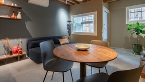 Ein modernes Wohnzimmer mit einem runden Holztisch, einem dunkelblauen Sofa und einem großen Fenster.