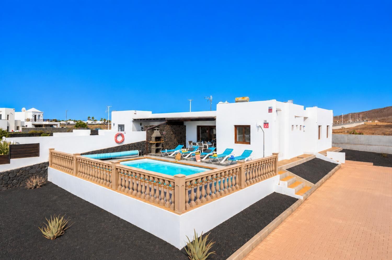 Un edificio moderno con piscina, sillas de descanso y un muro de piedra.