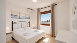 Ein Schlafzimmer mit einem Bett, Nachttischen, einem Fenster mit Vorhängen, einem Bild an der Wand und einer Deckenleuchte.