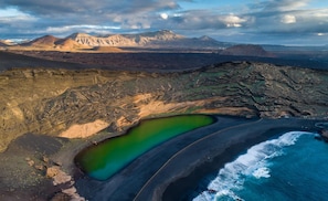 An aerial view of a coastal landscape with a green lagoon, rocky terrain, and distant mountains.