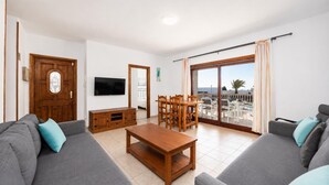 Ein Wohnzimmer mit einer Couch, einem Fernseher, einem Holzschrank und einem Balkon mit Gartenmöbeln.