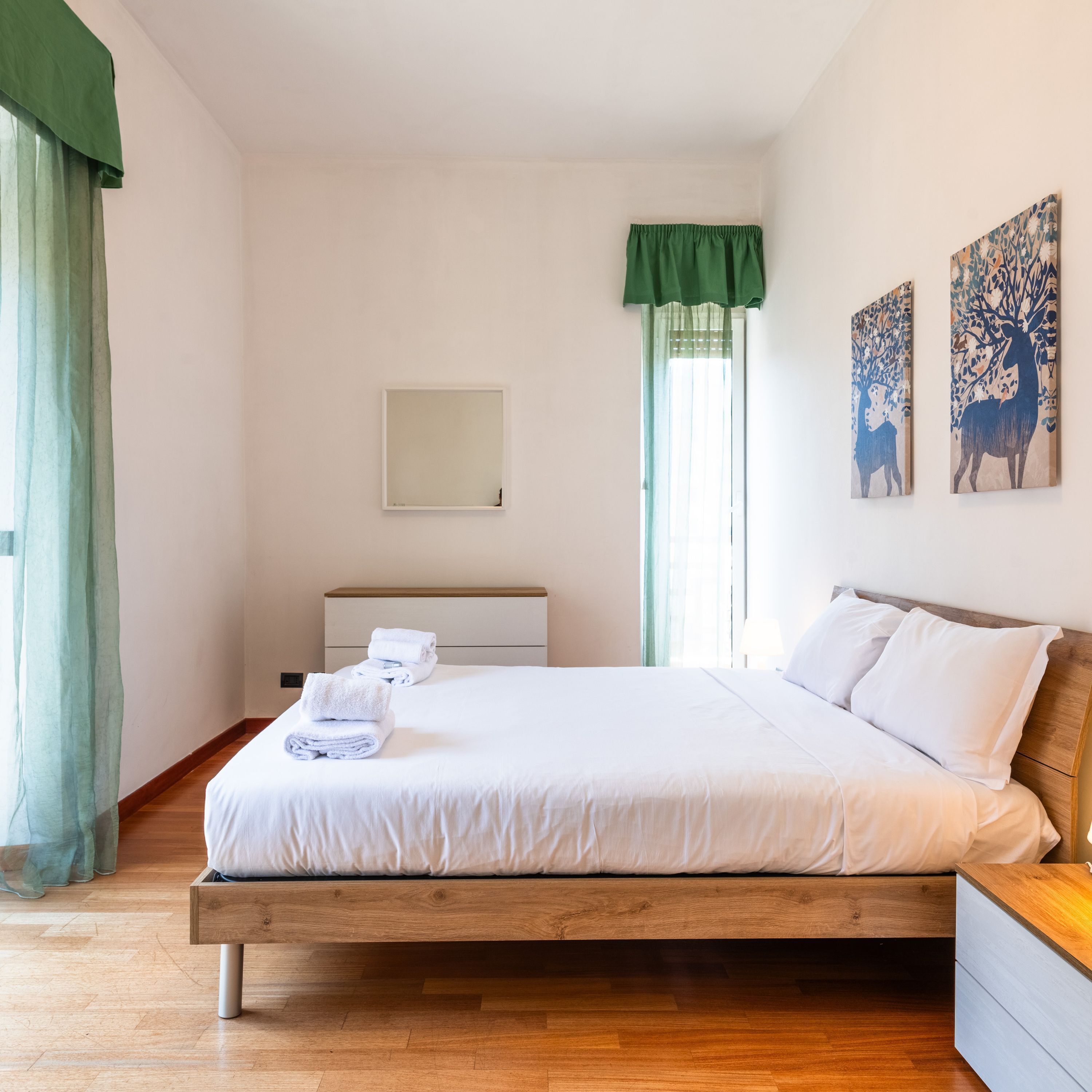 Een slaapkamer met een houten bed, een nachtkastje, een spiegel en twee aan de muur bevestigde schilderijen.