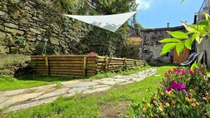 A stone pathway leading to a wooden bench area with a hammock, surrounded by lush greenery and flowering plants. - Secret Garden Suite- Bluchalet  (Riomaggiore)