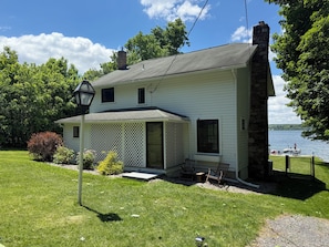 Une maison à deux étages dotée d’un porche couvert, d’une cheminée en pierre et offrant une vue sur un lac.