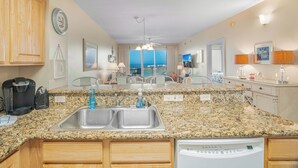 A kitchen with granite countertops, a double sink, wooden cabinets, a coffee maker, and a dishwasher. - Ariel Dunes II 708 *Stunning Beach Views*Pools* (Miramar Beach)
