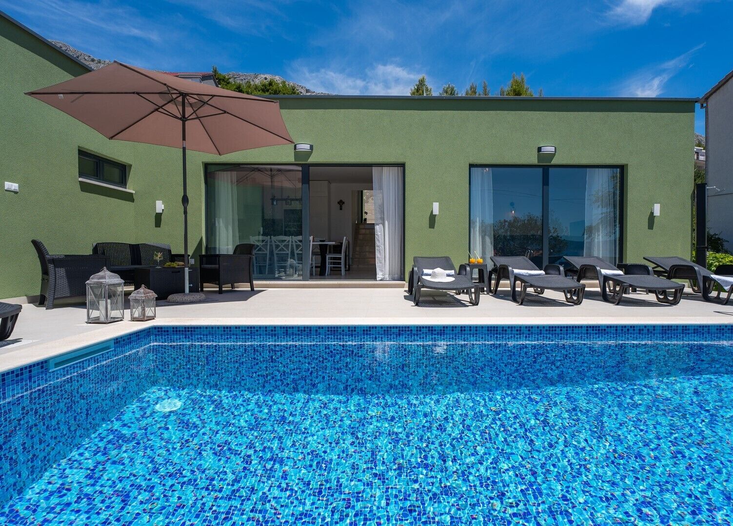 Un edificio moderno con piscina, area relax all'aperto e un grande ombrellone.