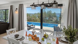 Un coin repas avec une table dressée pour quatre personnes, une vue sur une piscine et un balcon avec des sièges d’extérieur.
