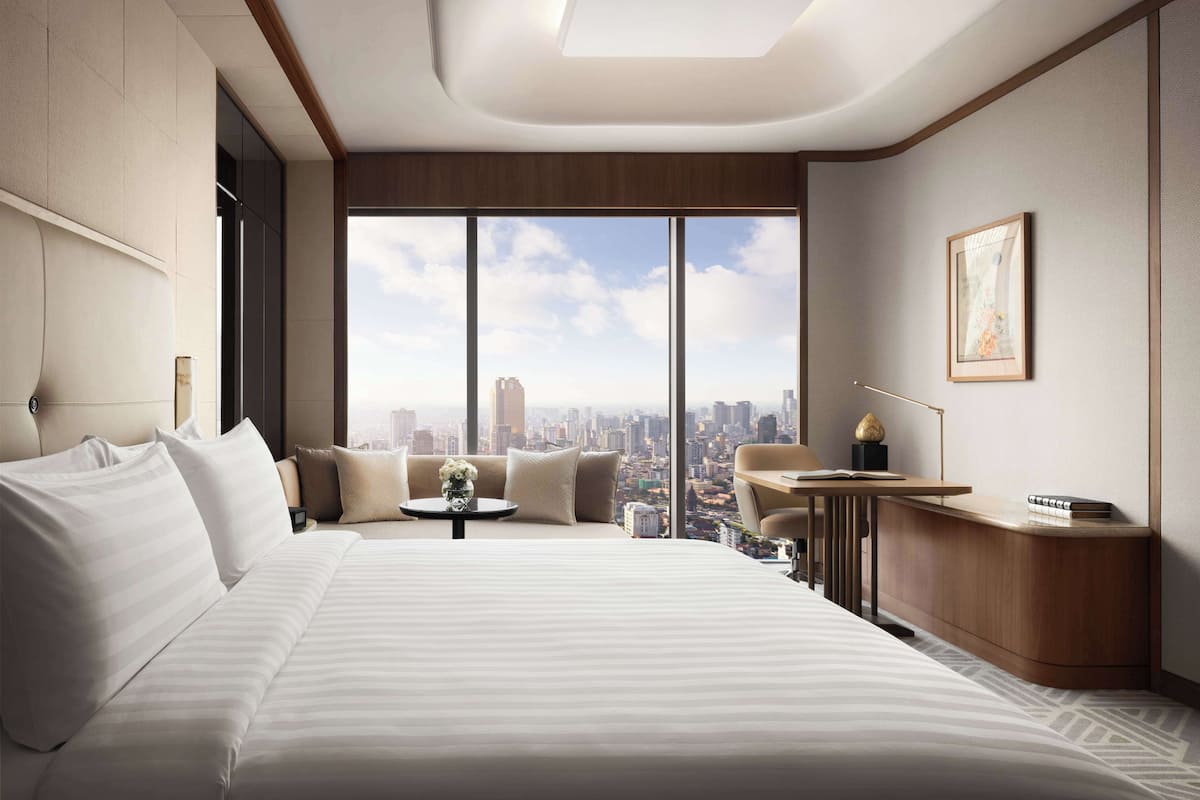 A modern hotel room with a large bed, a small desk, and a city view.