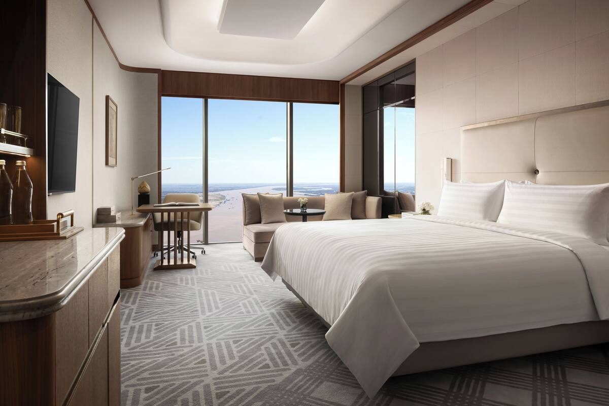 A modern hotel room with a large bed, a desk, and a view of the cityscape.
