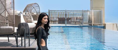 A pool area with a clear sky, lounge chairs, and a tiled deck.