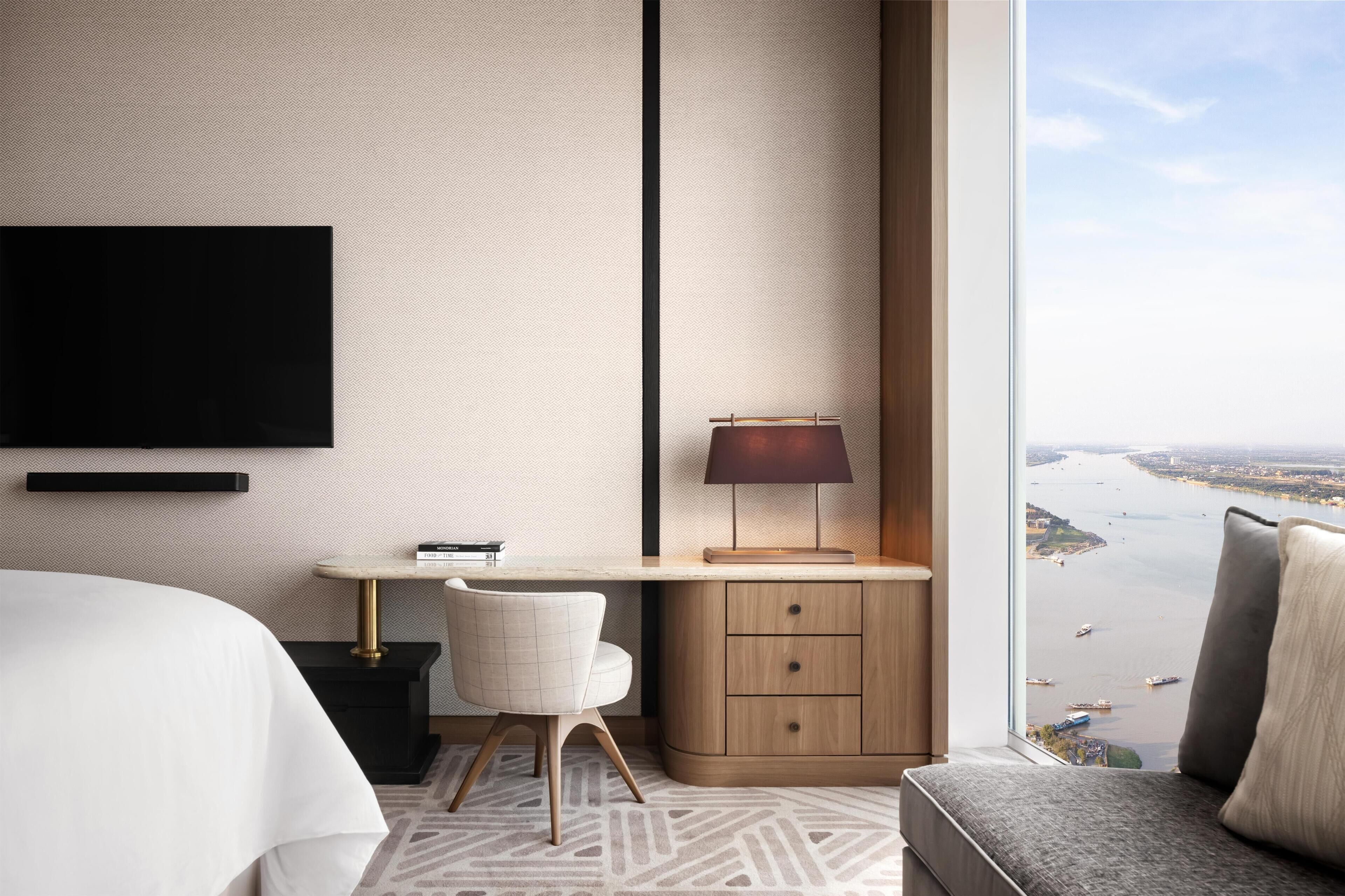 Ein modernes Hotelzimmer mit großem Fenster, Schreibtisch, Stuhl und Bett.