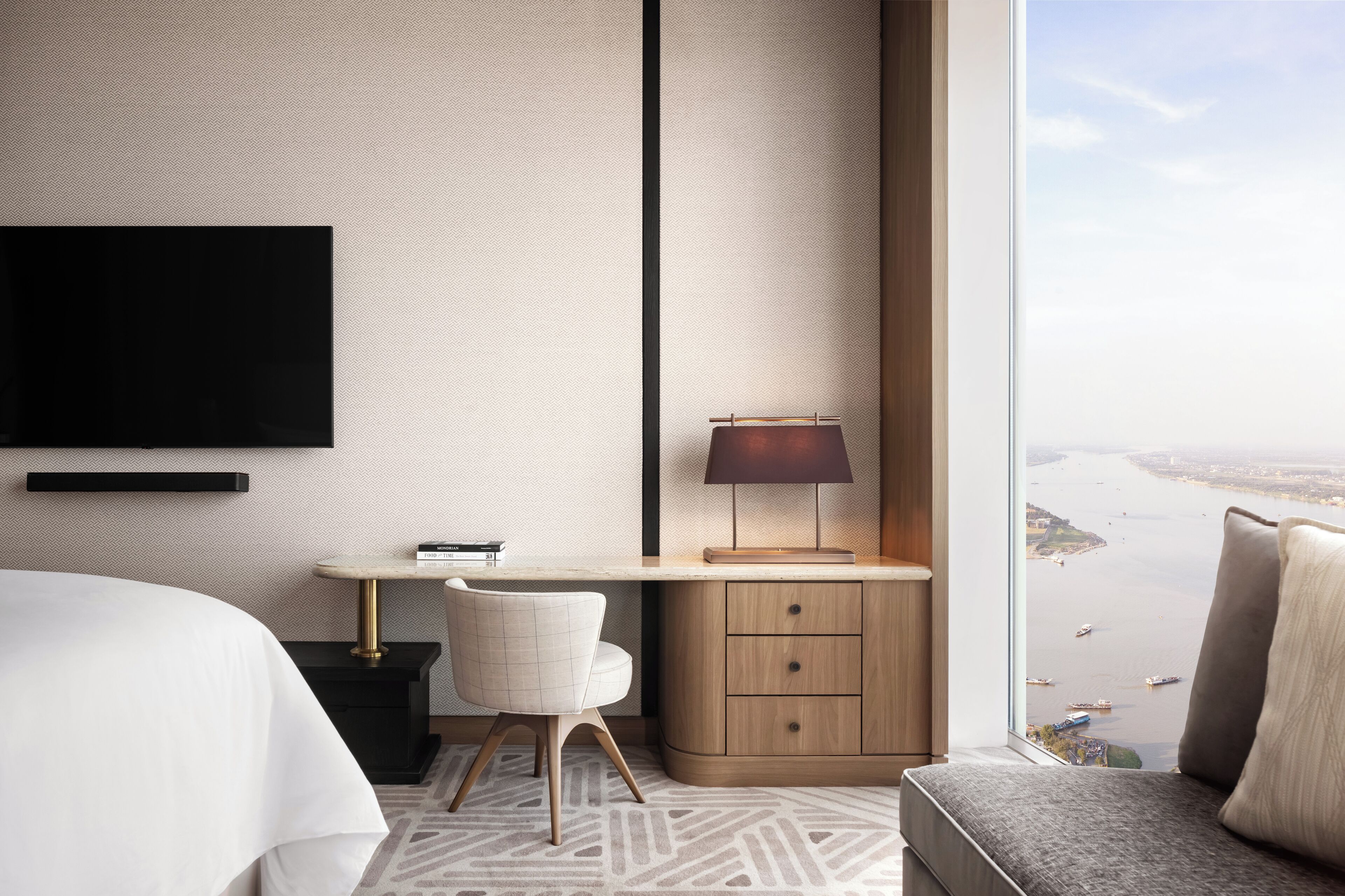 Habitación de hotel moderna con un ventanal grande, un escritorio con lámpara, una silla y una cama.