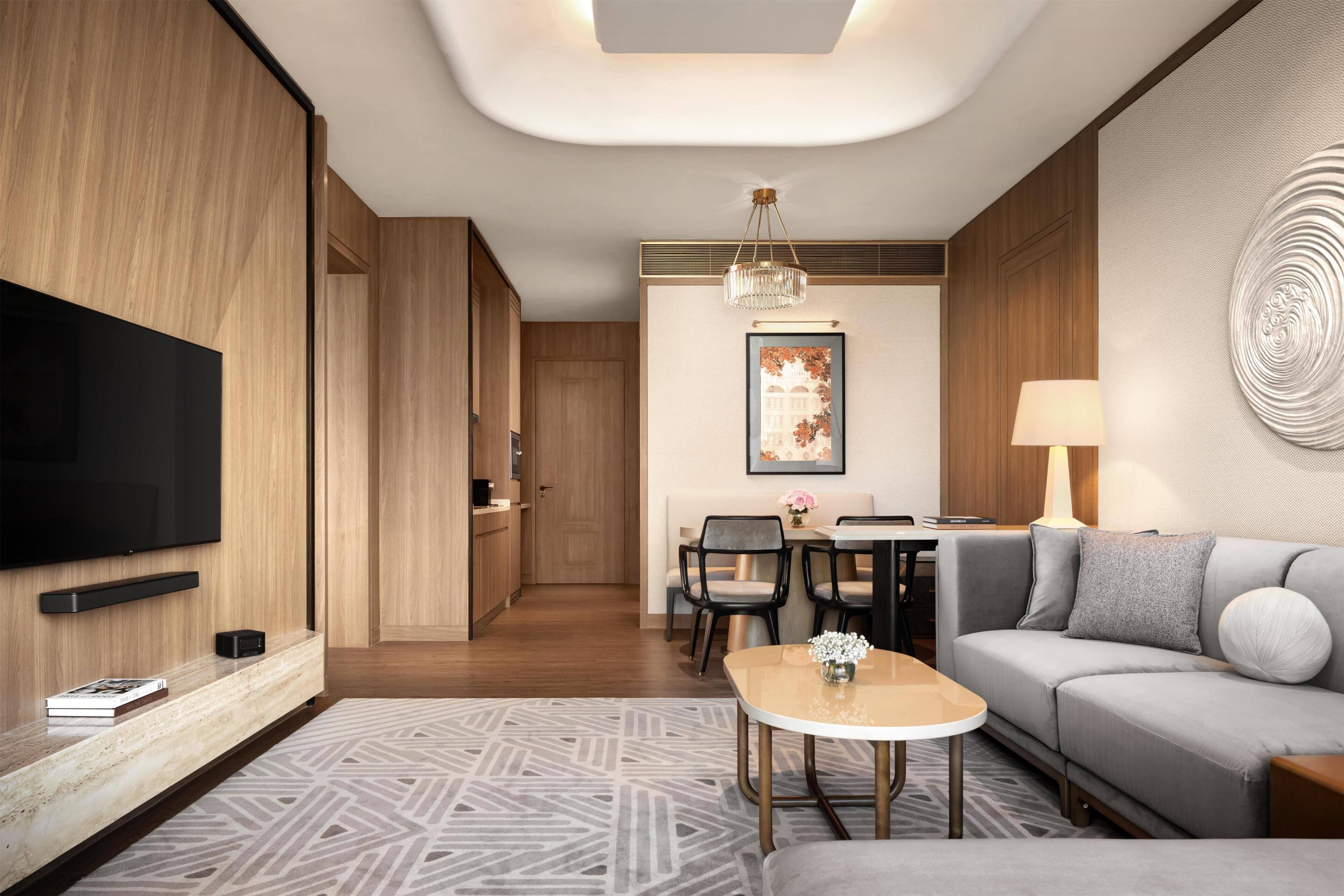 A modern living room with a flat-screen TV, a sofa, a dining table with chairs, and a patterned rug.