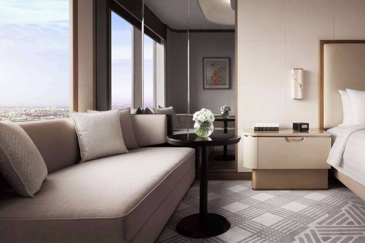 A modern hotel room with a sofa, a small table with a vase of flowers, a bedside table with a clock, and a bed.