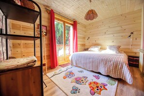 A cozy wooden cabin bedroom with a bed, a shelf, a window with curtains, and a hanging light fixture. - 🏡☀️ Chez Lily – Family House at the Foot of Le Criou 🌱⛰ (Samoëns)