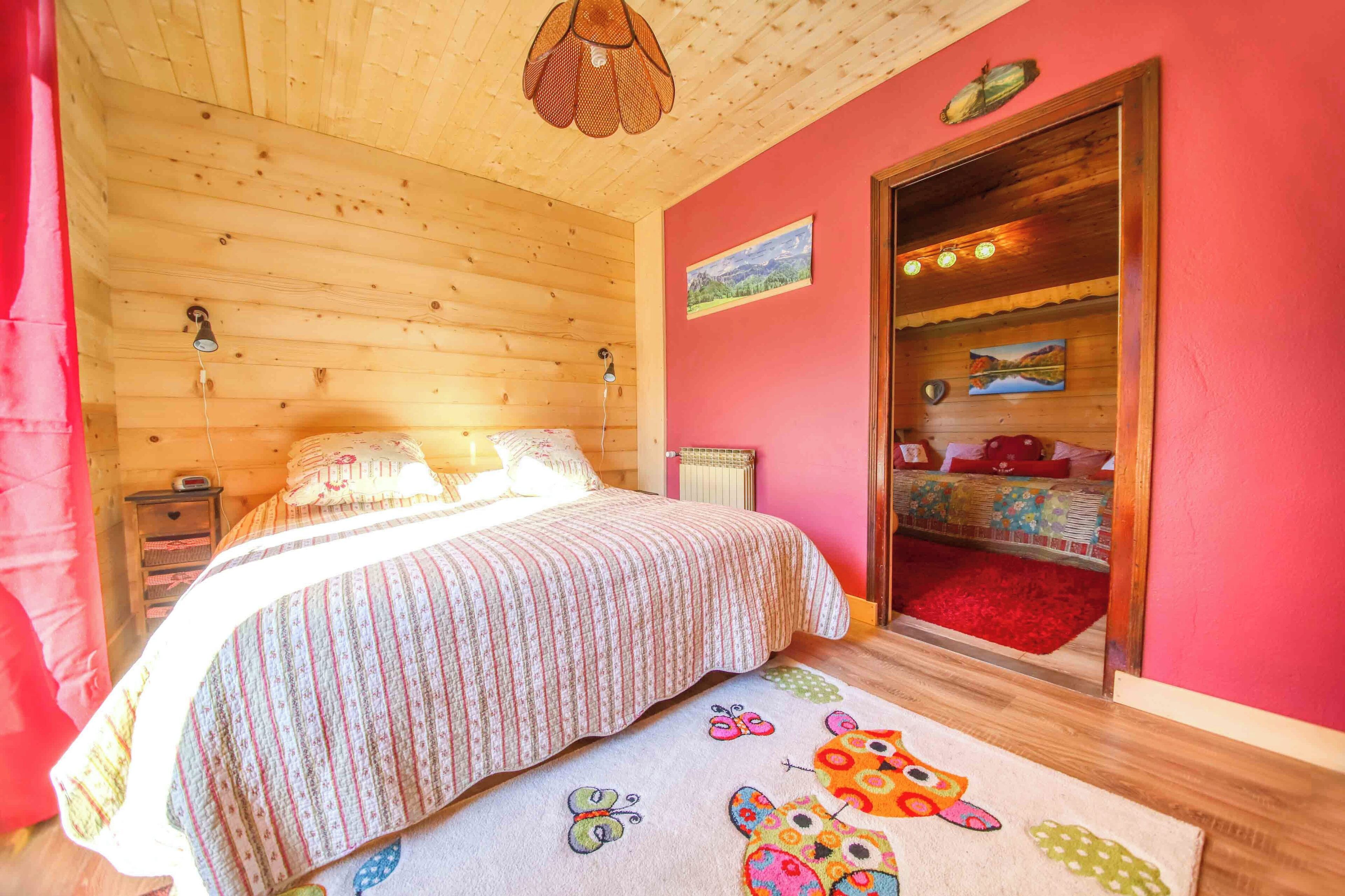 Een gezellige kamer met een houten plafond, een bed met gestreept beddengoed, een rood tapijt met een vlinderprint en een kast met rode binnenkant.