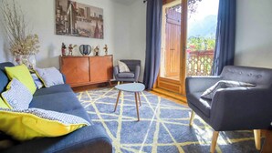 A living room with a sofa, armchair, and a small table. There is a cabinet with decorative items and a painting on the wall. - 🏡☀️ Chez Lily – Family House at the Foot of Le Criou 🌱⛰ (Samoëns)
