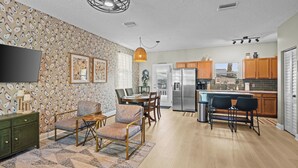 A modern kitchen with wooden cabinets, a stainless steel refrigerator, and a dining area with a table and chairs. - Southern Charmer|Private Backyard|Walk to Downtown (Saint Augustine)