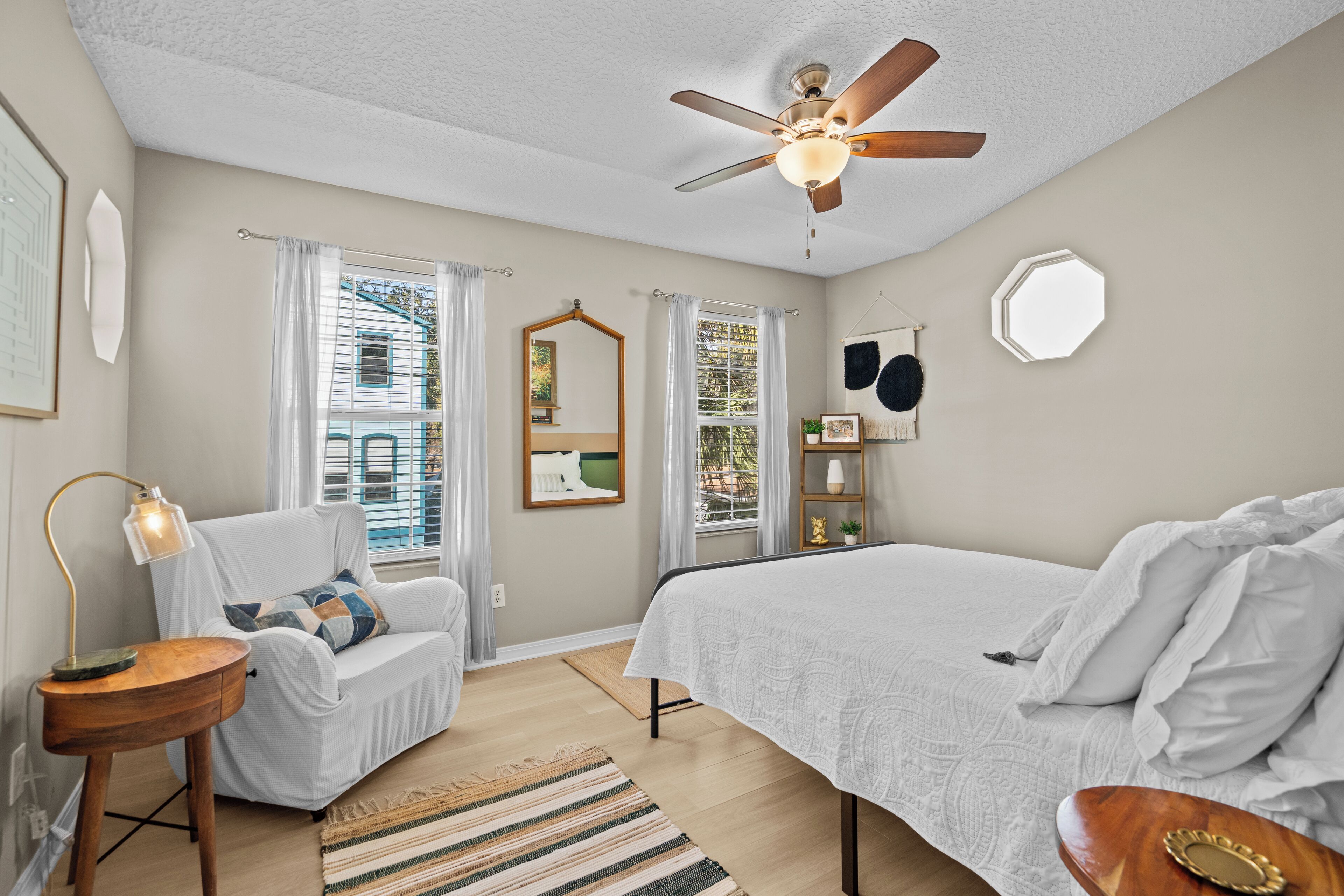 A bedroom with a bed, a chair, a desk, a ceiling fan, and a window with curtains.