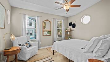 A bedroom with a bed, a chair, a desk, a ceiling fan, and a window with curtains.