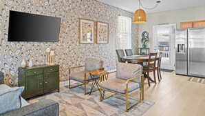 A modern living room with a flat-screen TV, patterned wallpaper, a green cabinet, and a dining area with a table and chairs. - Southern Charmer|Private Backyard|Walk to Downtown (Saint Augustine)