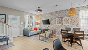 A modern living room with a sofa, dining table, chairs, and a TV mounted on the wall. - Southern Charmer|Private Backyard|Walk to Downtown (Saint Augustine)