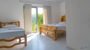 A bedroom with two wooden beds, white bedding, and a large sliding glass door leading to a balcony with a view of greenery. - Hotel Tintipan (Isla Tintipán)