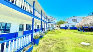 A building with a blue and white exterior, a covered outdoor area with a thatched roof, and a well-maintained lawn. - Hotel Tintipan (Isla Tintipán)