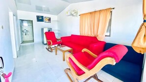 A modern living room with a red sofa, a blue sofa, and a wooden rocking chair. There is a small table and a fan on the wall. - Hotel Tintipan (Isla Tintipán)