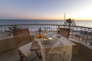 A balcony with a table set for two, overlooking the ocean at sunset.