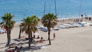 A beach with palm trees, people sunbathing, and boats lined up on the sand. - Breathe, 100% Mediterranean. Mandala apARTments (Calafell)