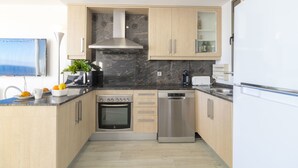 A modern kitchen with wooden cabinets, a built-in oven, a dishwasher, and a marble backsplash. - Breathe, 100% Mediterranean. Mandala apARTments (Calafell)