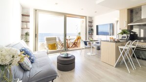 A modern living room with a sofa, coffee table, and a view of the ocean through large glass doors. - Breathe, 100% Mediterranean. Mandala apARTments (Calafell)