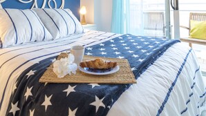 A neatly made bed with a star-patterned blanket, a plate with croissants and coffee, and a wicker placemat. - Breathe, 100% Mediterranean. Mandala apARTments (Calafell)