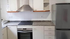 Keittiössä on valkoiset kaapit, ruostumattomasta teräksestä valmistettu liesituuletin, sisäänrakennettu uuni ja jääkaappi.